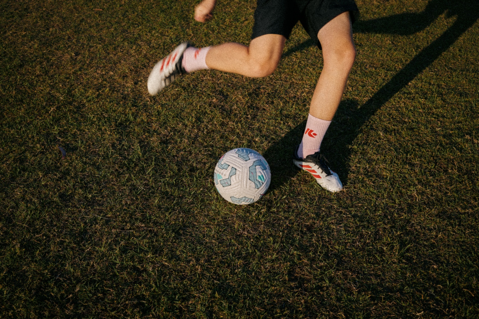 Athlete in custom Kaizen socks running with a ball on grass at golden hour